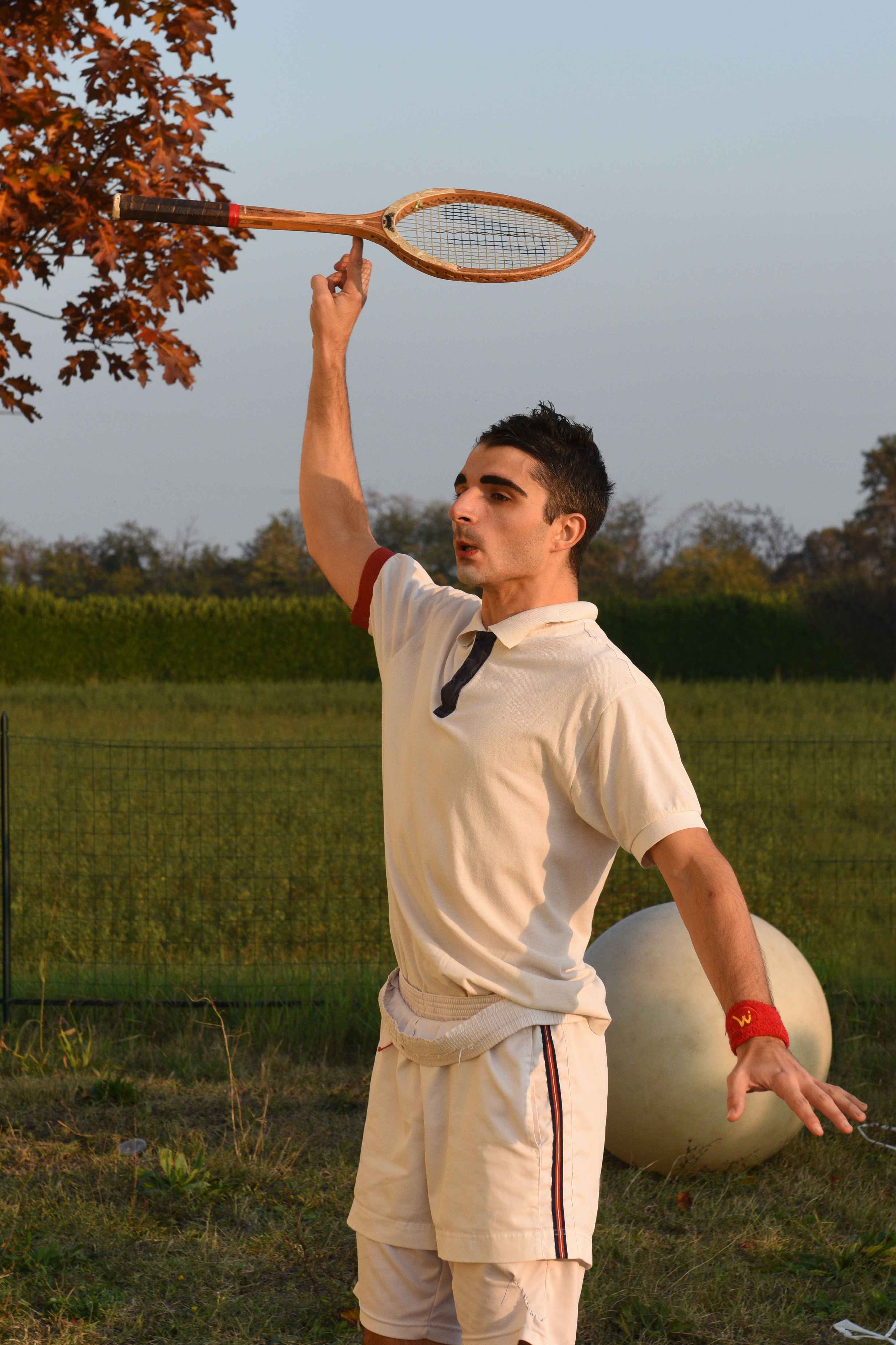 Un clown tennista tiene in equilibrio una racchetta da tennis su un dito.